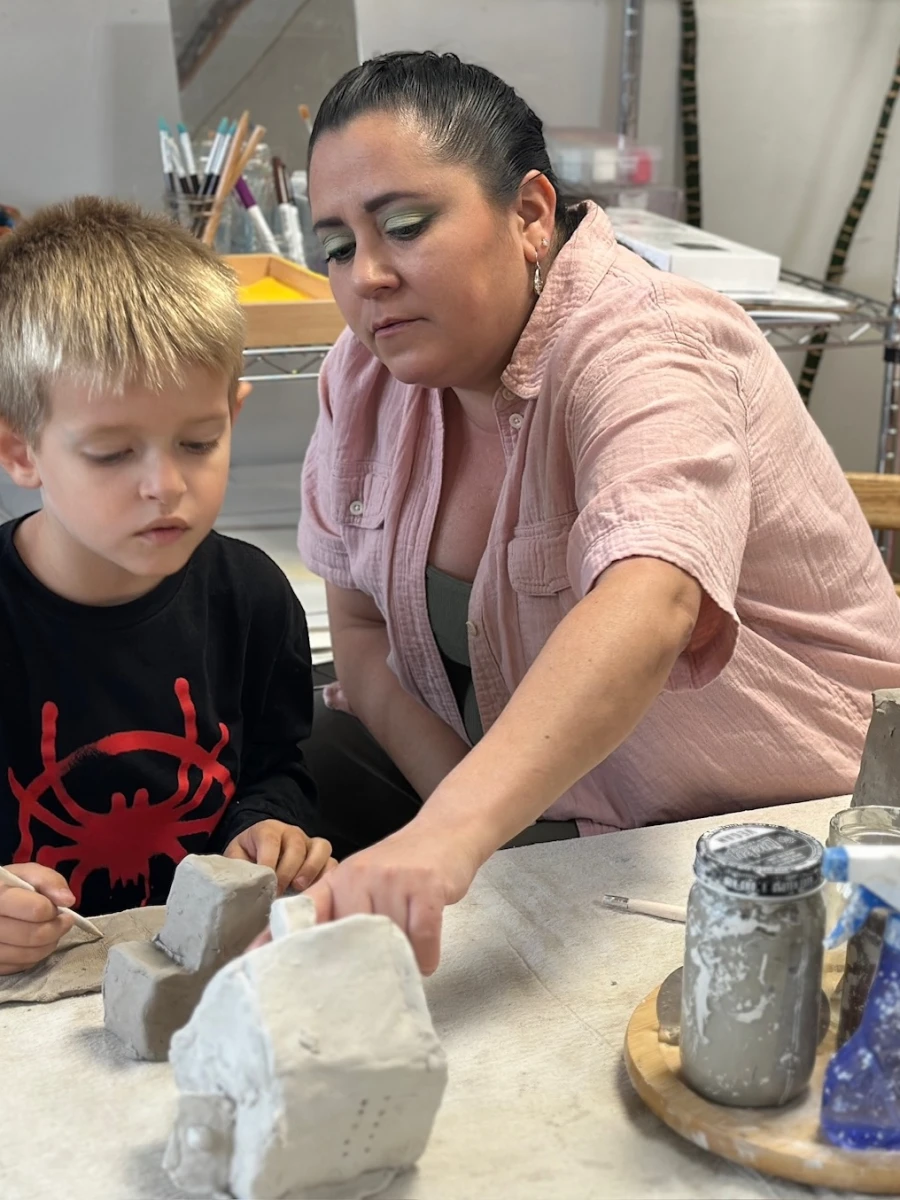 An educator guiding and scaffolding a child as they work on a clay house they created.