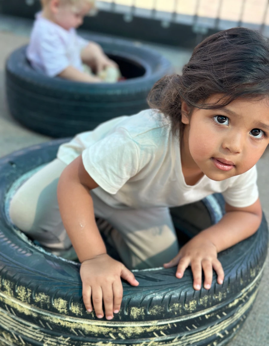 A child perched in a tire, looking up at the viewer with curiosity and wonder