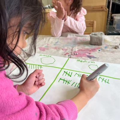 A child carefully adding tally marks to a large sheet of paper, used to count the number of clay balls they’ve made in large, medium, and small sizes.