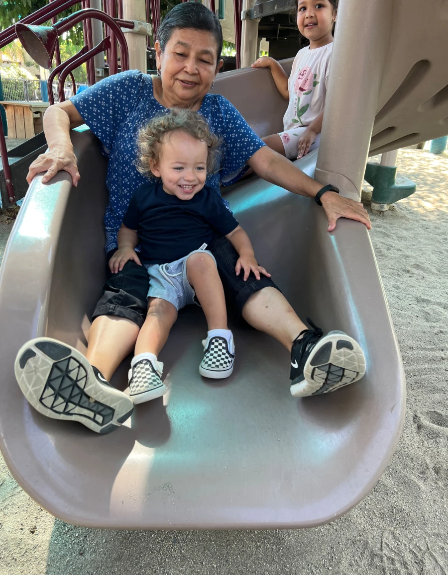 Two children joyfully sliding down a curly slide alongside one of their educators, sharing laughter and a playful moment together.