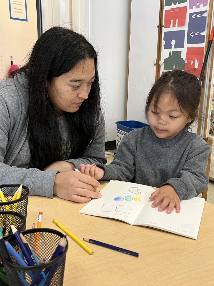 An educator supporting a child as they work on a journal entry.