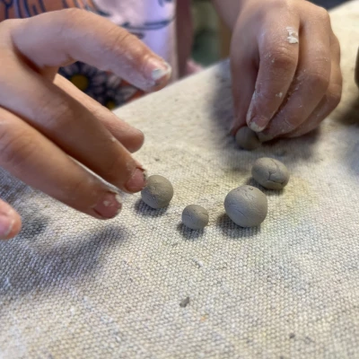 Hands of a child working with clay, carefully shaping it into different-sized balls at the clay table.