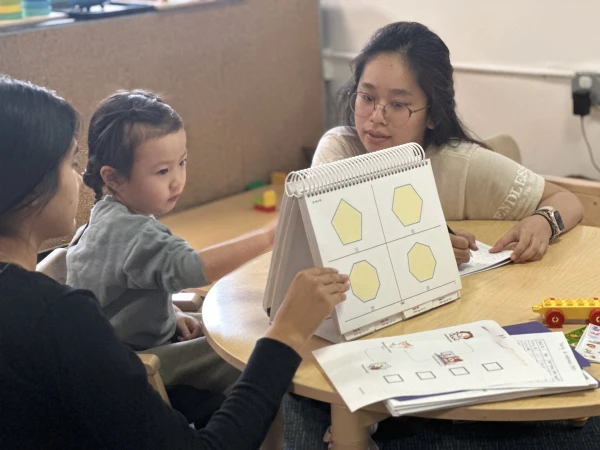 Shows a young child completing an assessment being conducted by two individuals, capturing a moment of focus and interaction.