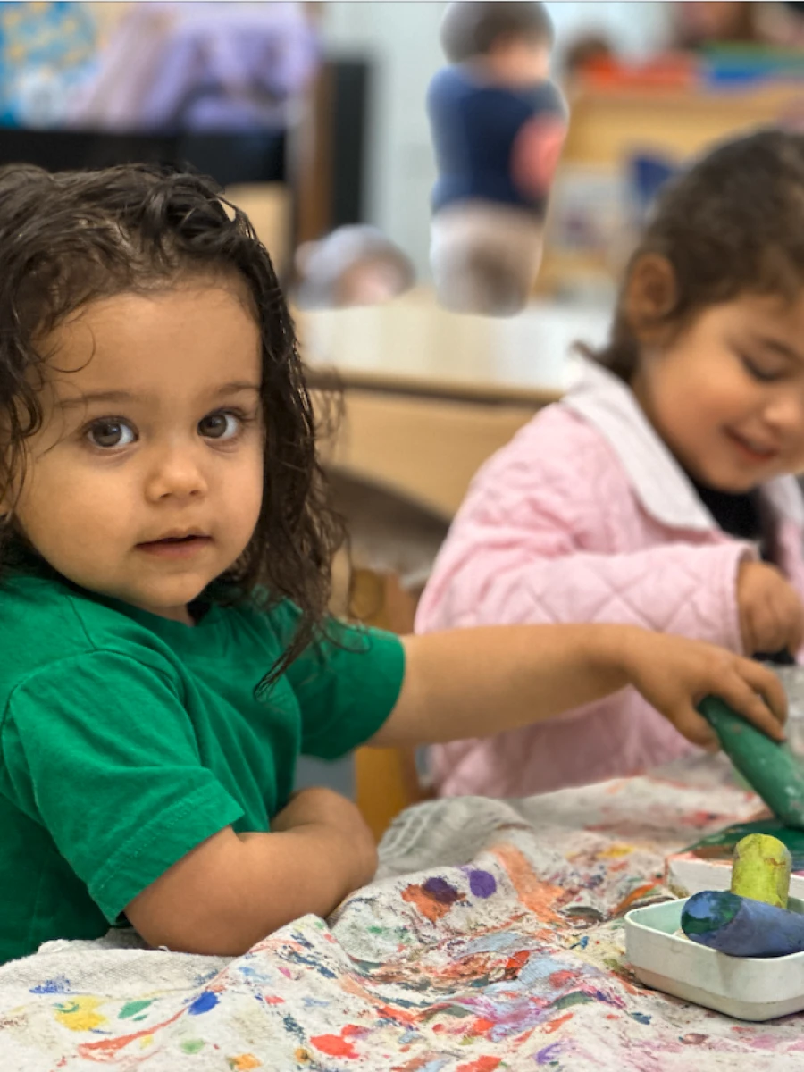 Two children working with vibrant blue and green tempera sticks on a collaborative canvas, creating art together.